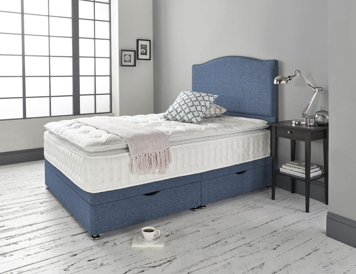 Blue upholstered bed with white mattress in a room with a window and side table.